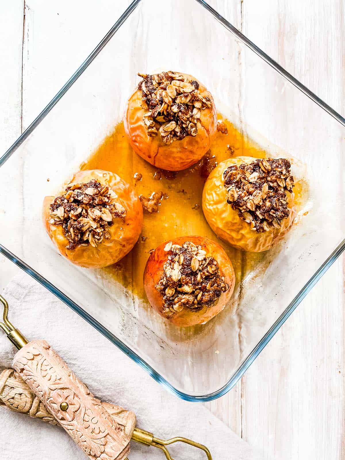 Four baked apples in a glass dish on a white table. 