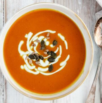 A bowl of soup with pumpkin seeds on a white table.