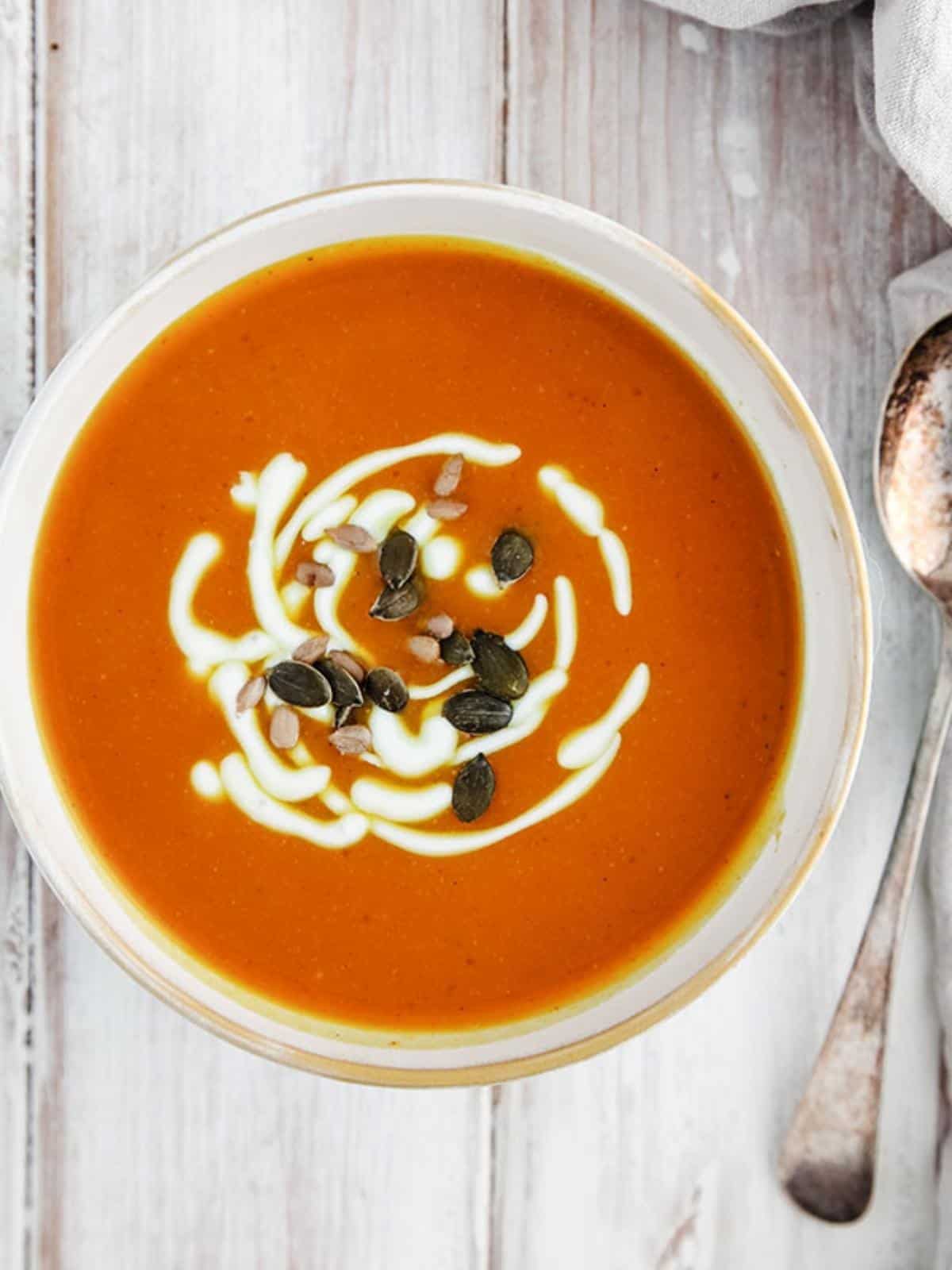 A bowl of soup with pumpkin seeds on a white table.