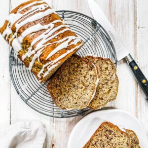 Sliced banana bread drizzled with white icing on a wire rack.