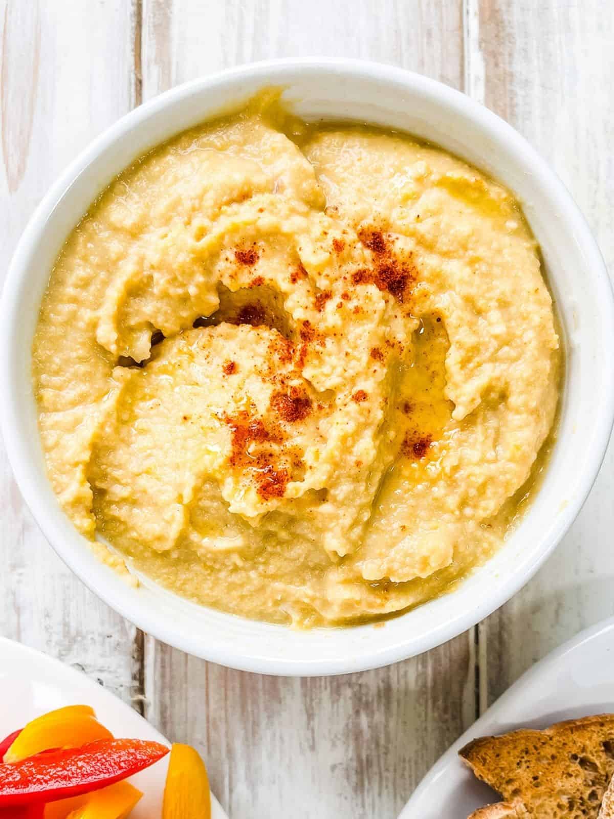 A white dish of hummus on a white table.
