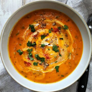 A bowl of carrot and coriander soup on a white table.