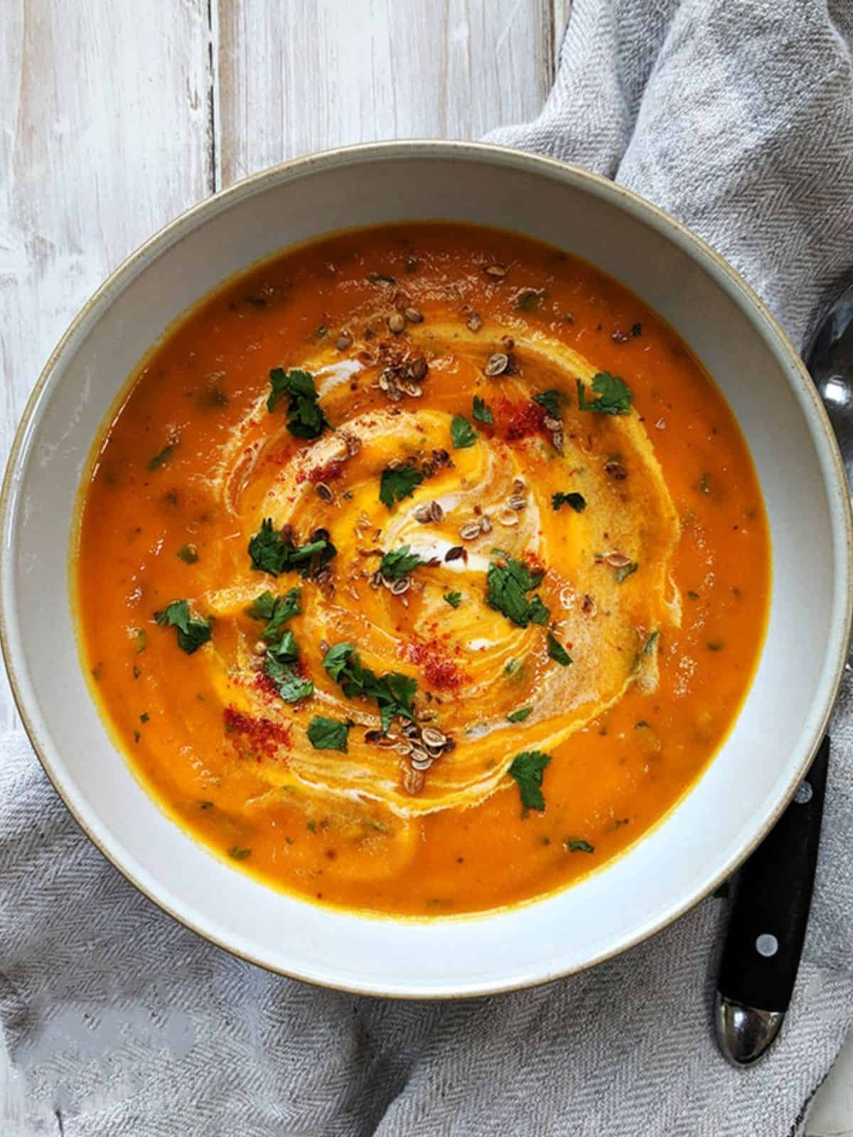 A bowl of carrot and cilantro soup on a white table. 