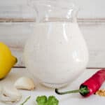 A glass jug of creamy dressing with lemon, garlic, cilantro and chili on the side