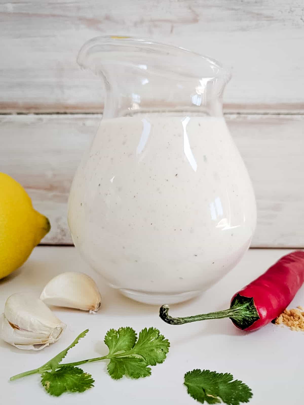 A glass jug of creamy dressing with lemon, garlic, cilantro and chili on the side