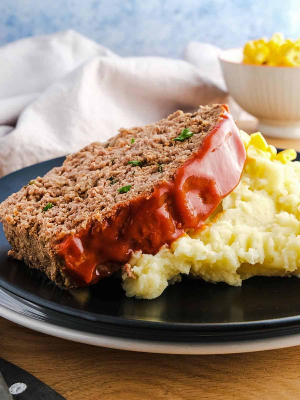 A slice of low calorie meatloaf on some mashed potato on a black plate.