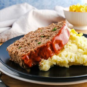 A s;lice of meatloaf topped with red sauce on a bed of mashed potato.