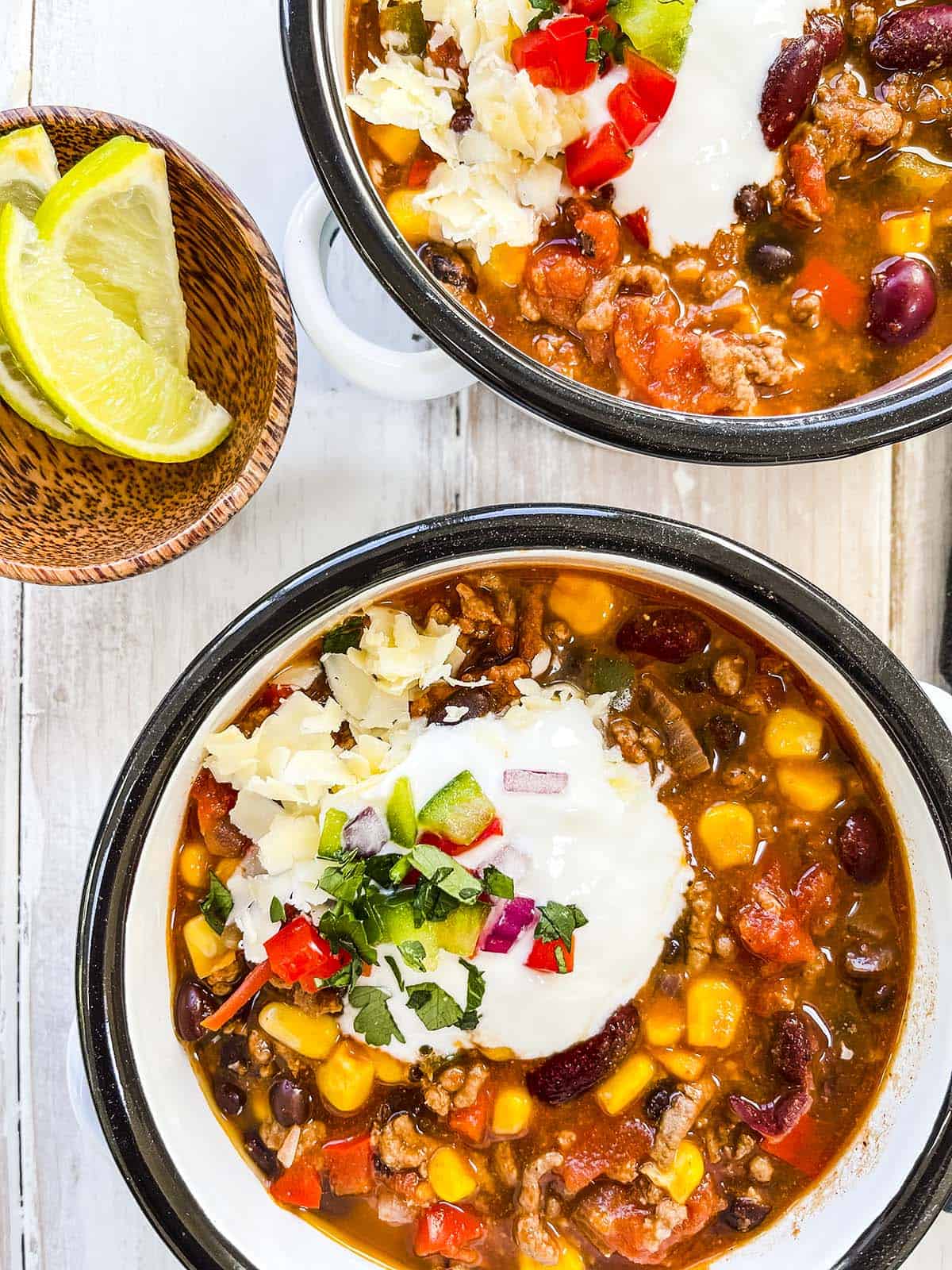 Taco soup in black rimmed bowls on a white wooden table.