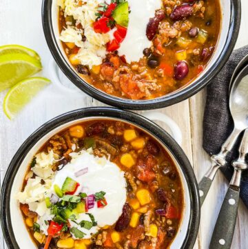 Two bowls of low calorie taco soup on a white table.